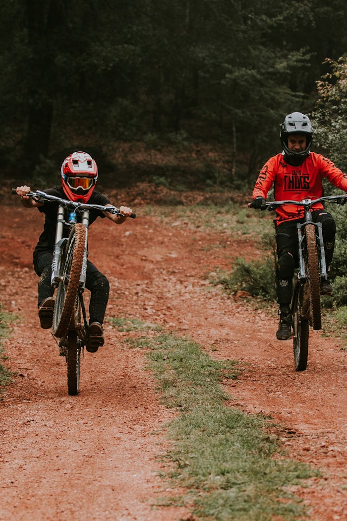 Two mountain bikers in protective gear riding on a forest dirt trail, showcasing their skills.
